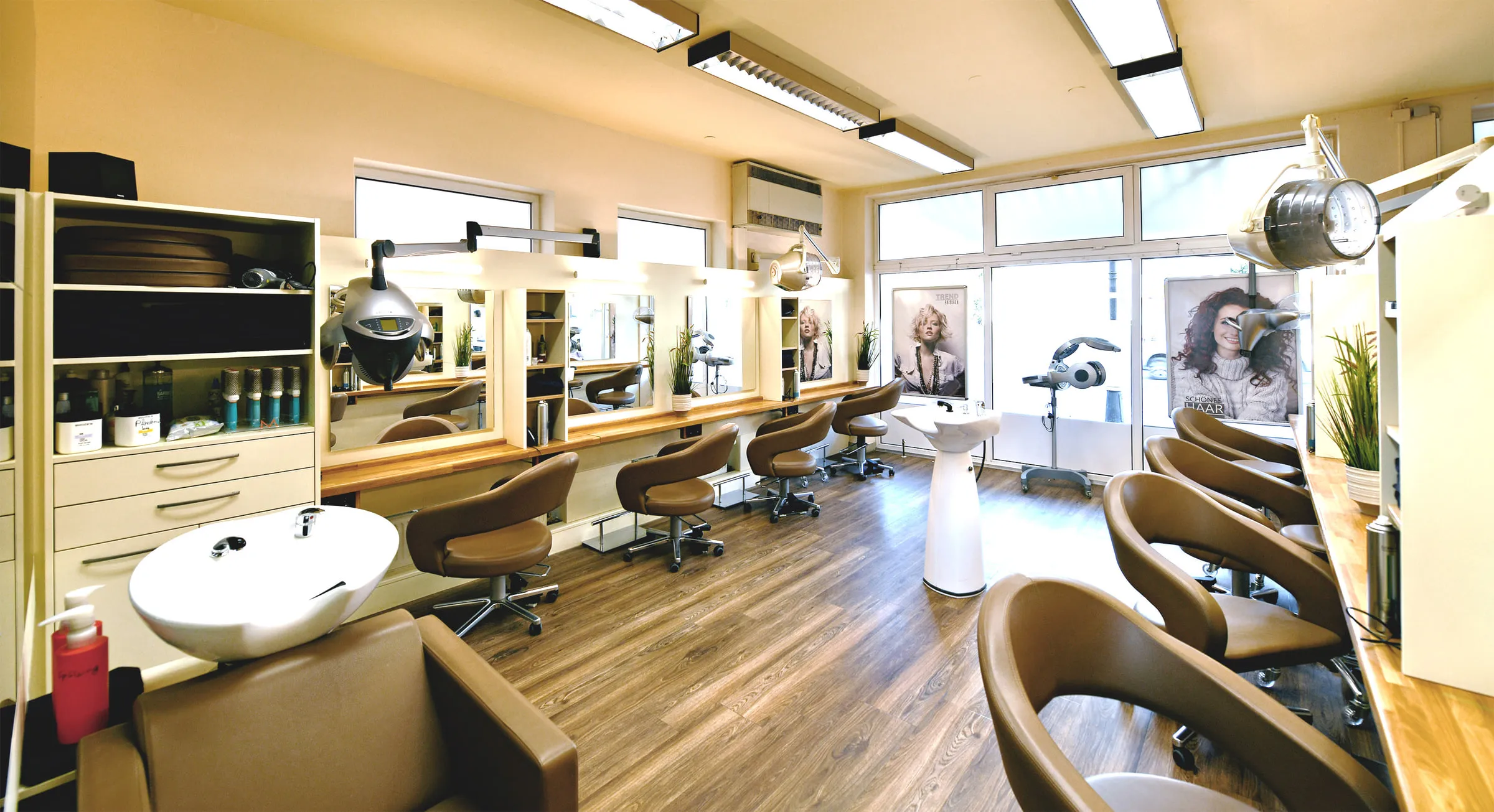 Blick in den Salon: helle Wände, Frisierplätze mit Spiegeln, braune Ledersessel und Holzboden